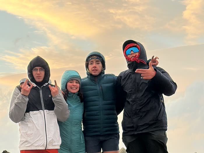 Cuatro abrigados en la cima con el cielo del atardecer