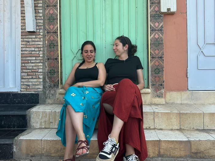 Dos amigas sentadas en el escalón de una puerta verde