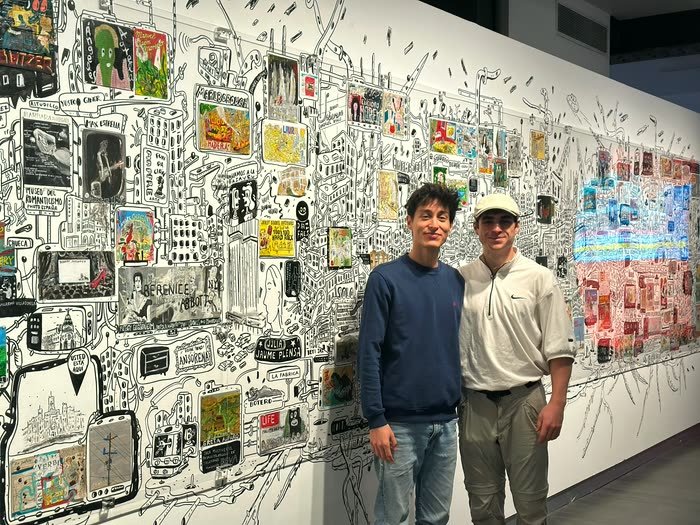 Dos posando delante de un mural enorme lleno de dibujos