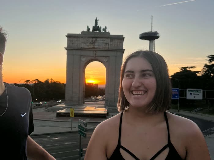 Una chica sonriendo con el Arco de la Victoria al atardecer