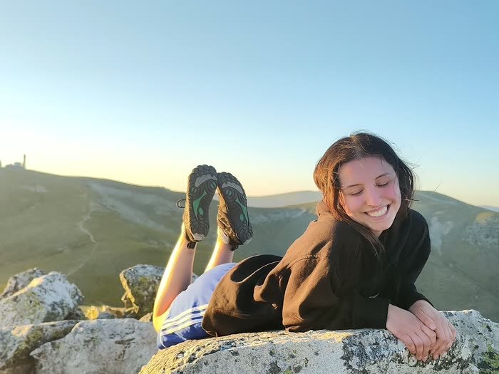 Una chica tumbada en una roca, sonriendo, con la sierra detrás